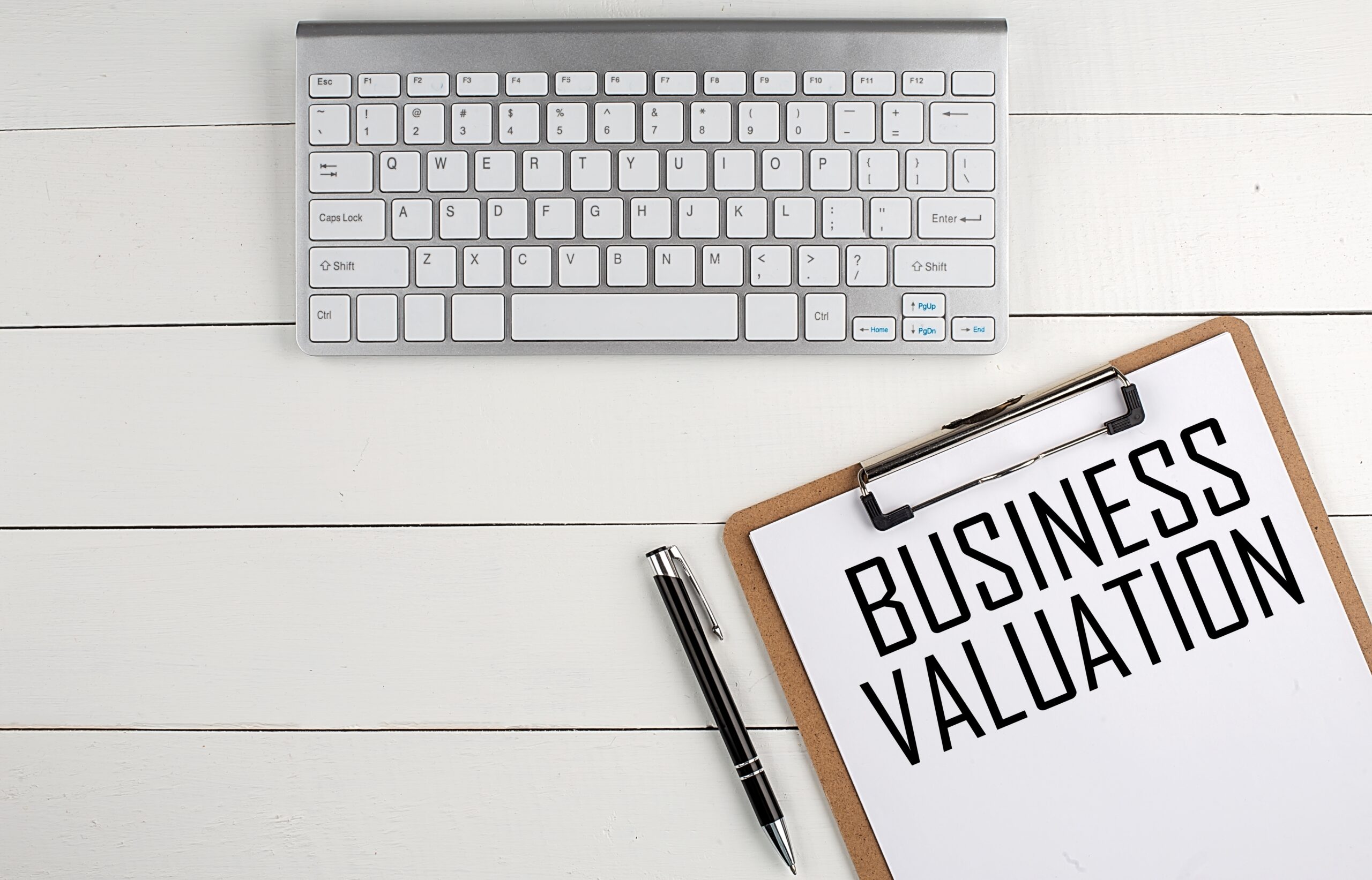 Professional desk with keyboard, clipboard displaying "Business Valuation" text, and pen – symbolizing business exit planning and valuation services.